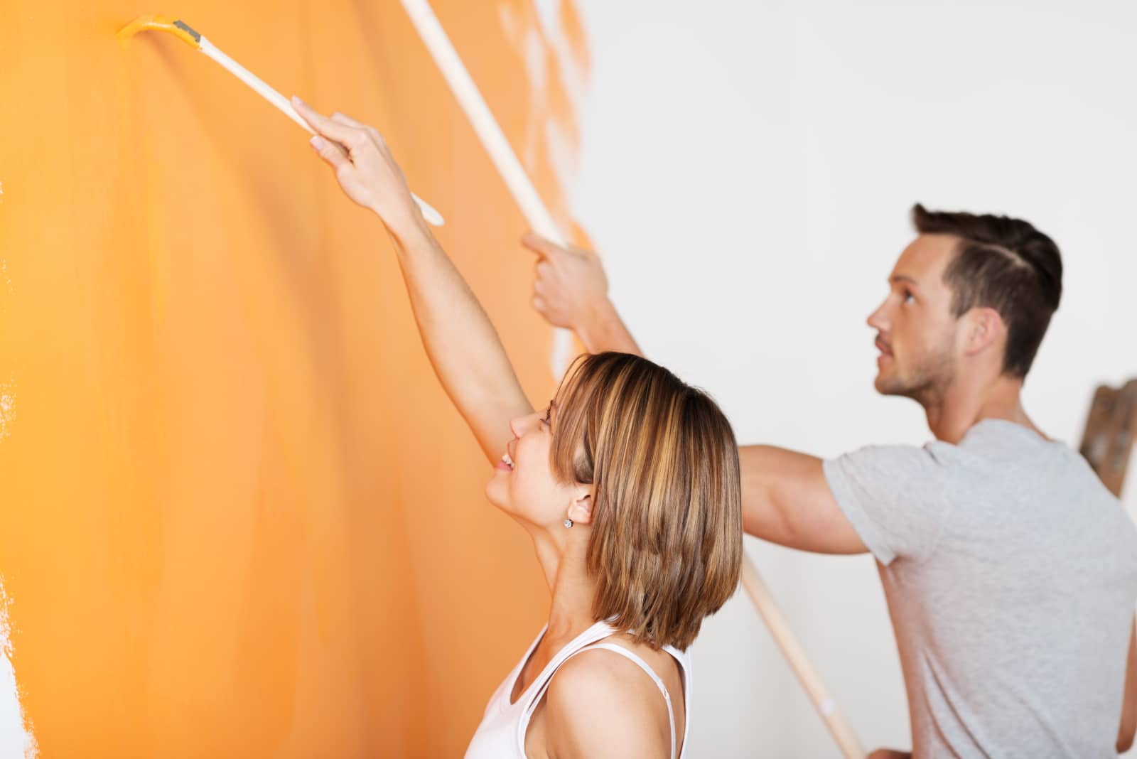 renovierung2 Junges Paar streicht eine weiße Wand mit Pinsel in der Farbe orange