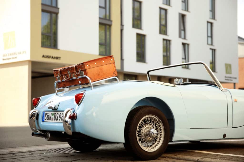 Hotel Landau Oldtimer Hellblaues Oldtimer-Cabrio mit braunem Lederkoffer auf dem Gepäckständer steht vor dem Hoteleingang des Maximilian Boutique-Hotels in Landau in der Pfalz