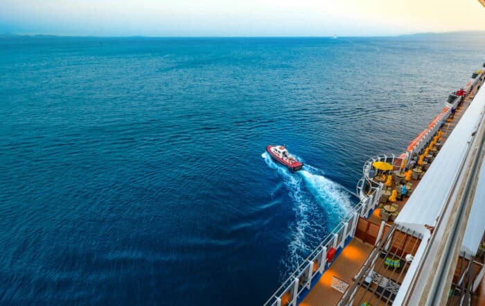Blick vom Kreuzfahrtschiff auf das blaue Meer und das abfahrende Beiboot