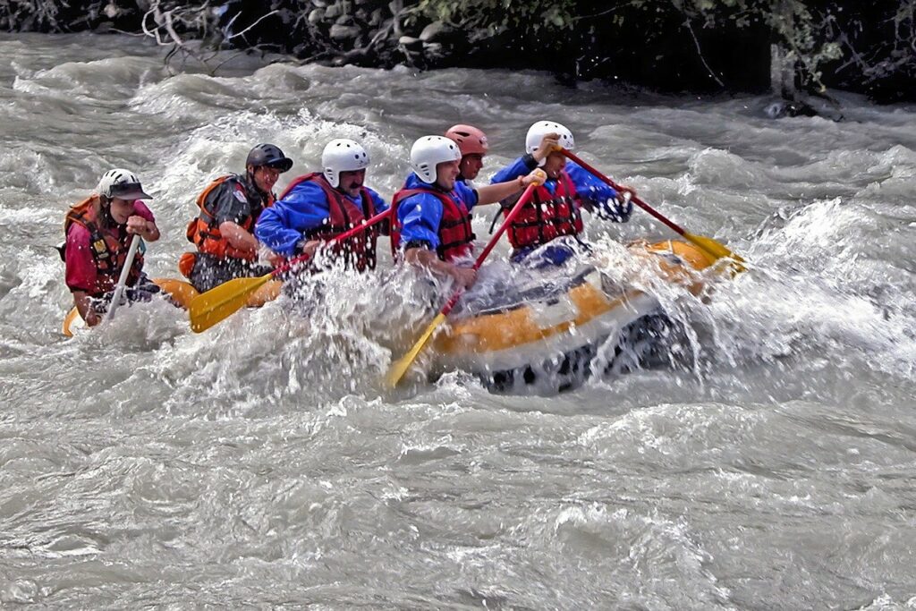 Rafting 5 Männer und eine Frau rudern in einem Raftingboot durch starke Strömung