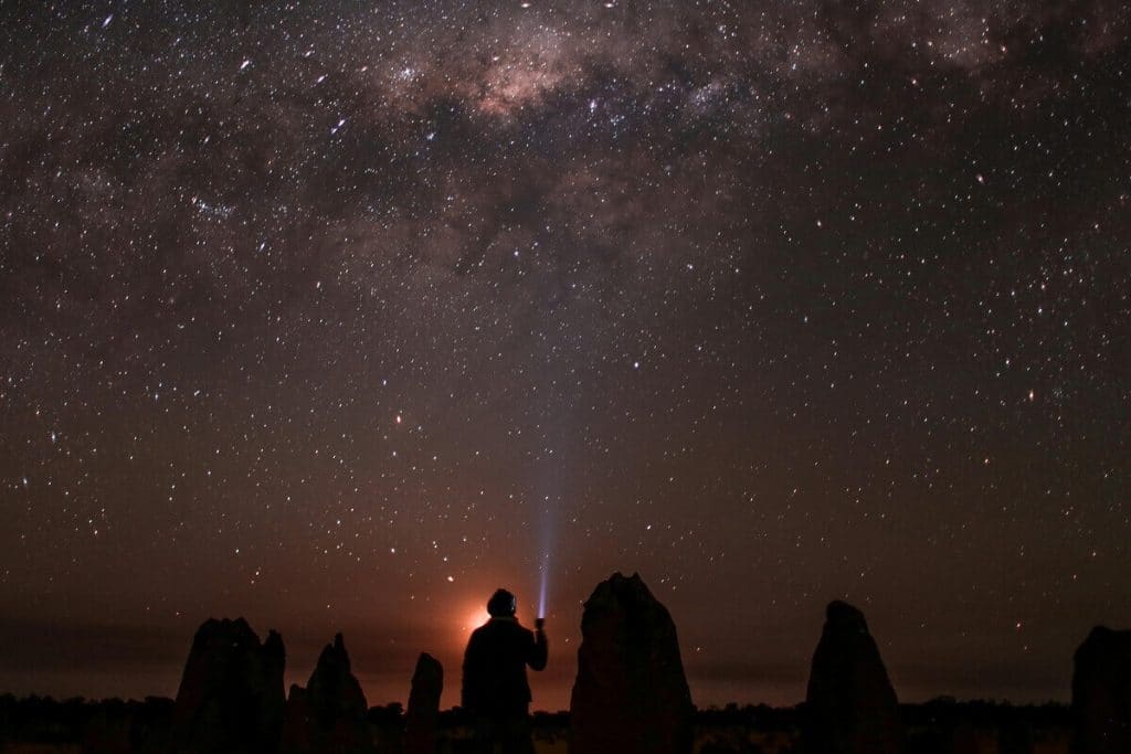 Romantische-Date-Tipps Person mit Taschenlampe leuchtet in den nächtlichen Sternenhimmel vor inmitten außergewöhnlihcer Felsen