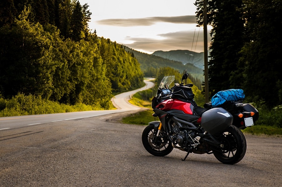 Motorrad mit Gepäck steht auf einer Landstraße, umgeben von grünen Wäldern und Bergen im Hintergrund.