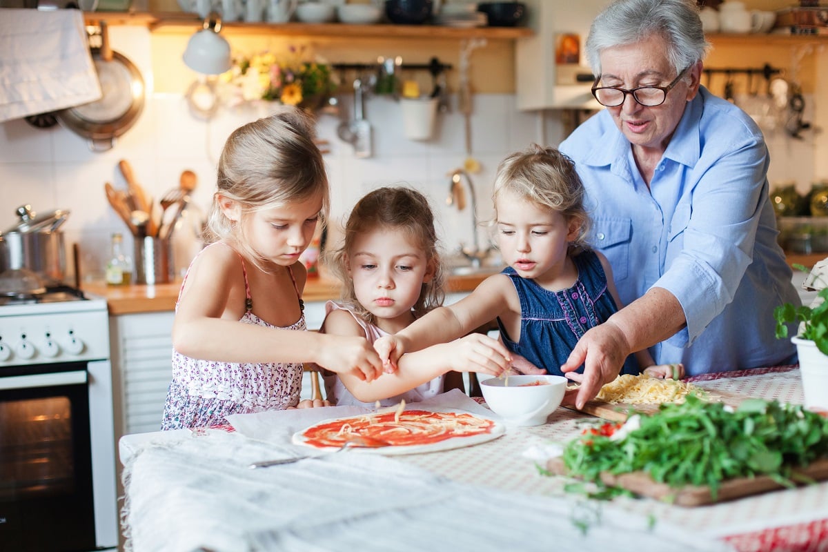 Familie mit Kindern und Großmutter bereitet Pizza zu - Kochen mit Kindern