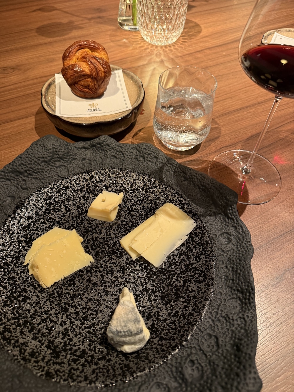Gourmetrestaurant Schote- Käseauswahl 4 verschiedene Käsesortena aus Schieferteller auf Holztisch mit Wasserglas und Rotweinglas