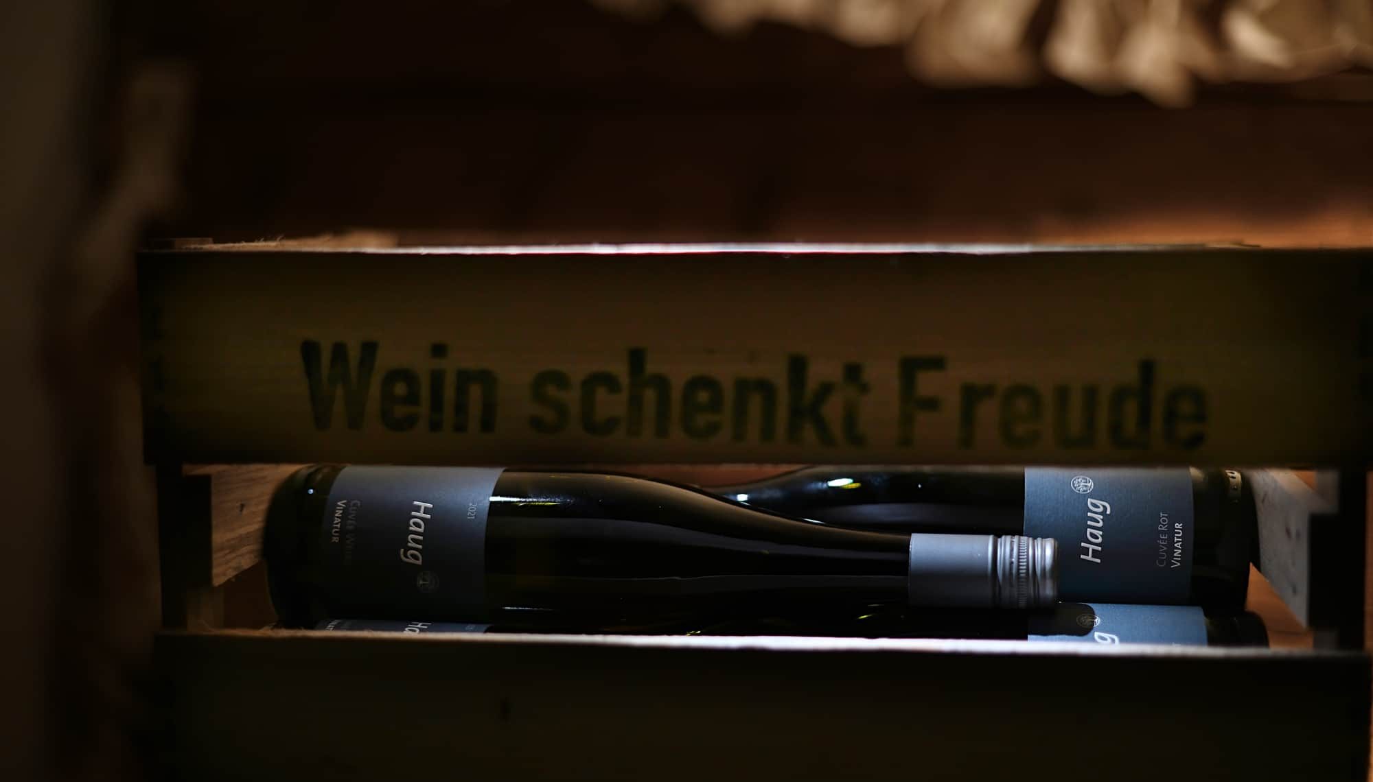 Etiketten Weingut Haug 2 Weinflaschen des Weinguts Haug liegen in einer Holzkiste auf der Steht - Wein schenkt Freude