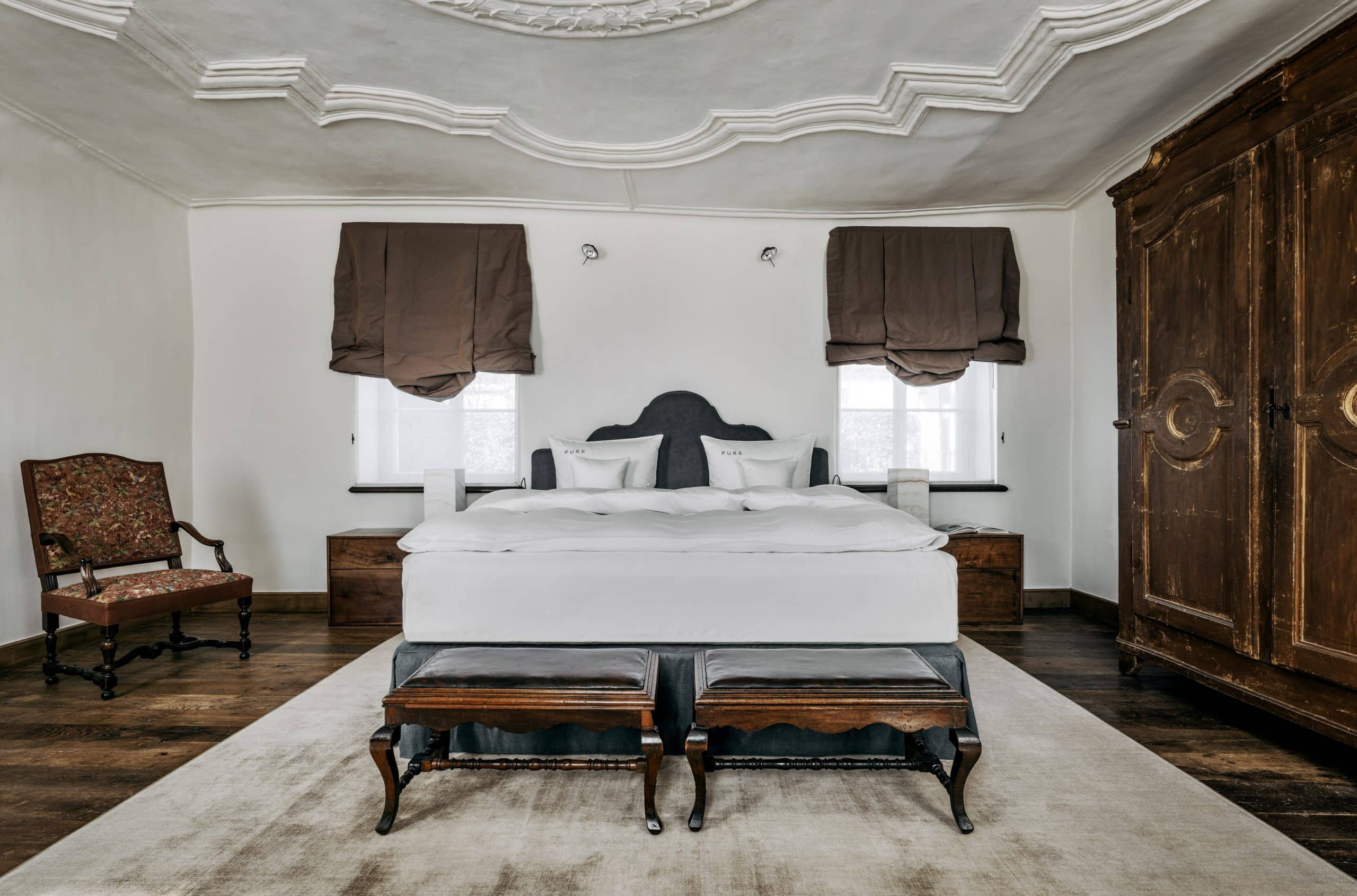 Signatur Suite SSAK_purs-2 großes Bett mit weißer Bettwäsche auf dunklem Holzboden mit antikem Schrank aus dunklem Holz, Stuckdecke in der Signature Suite im PURS in Andernach