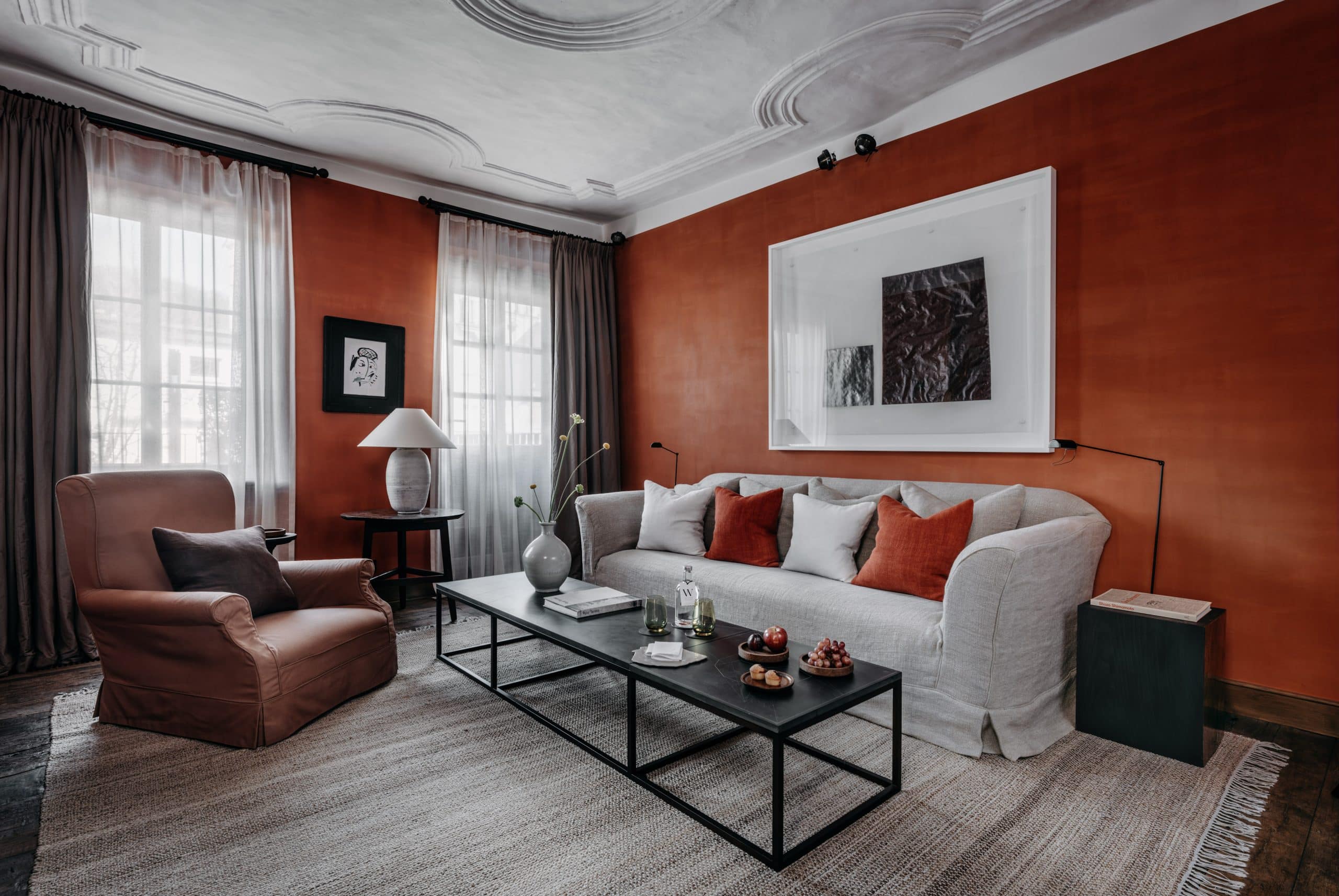 Signatur Suite SSAK_purs Signature Suite mit roter Wand, weißen Stuckdecken Sprossenfenster mit bodentiefen Vorhängen, Glastisch, Lampe und weißem Sofa in der Alten Kanzlei im PURS Andernach