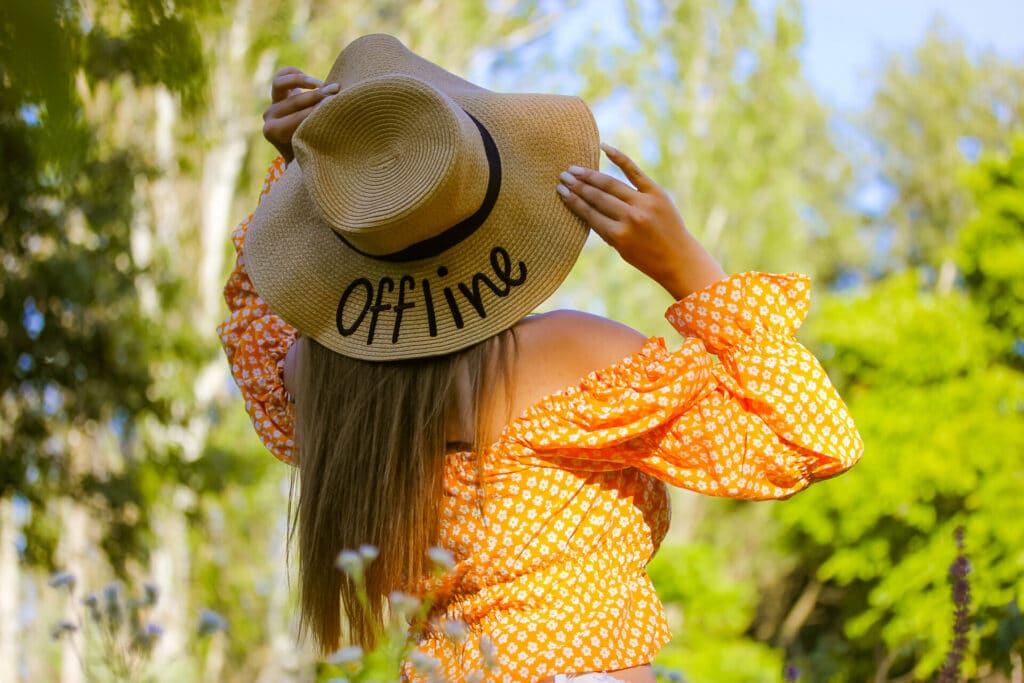 Digital Detox Junge Frau im Sommer mit Strohhut der die Aufschrift "offline" trägt