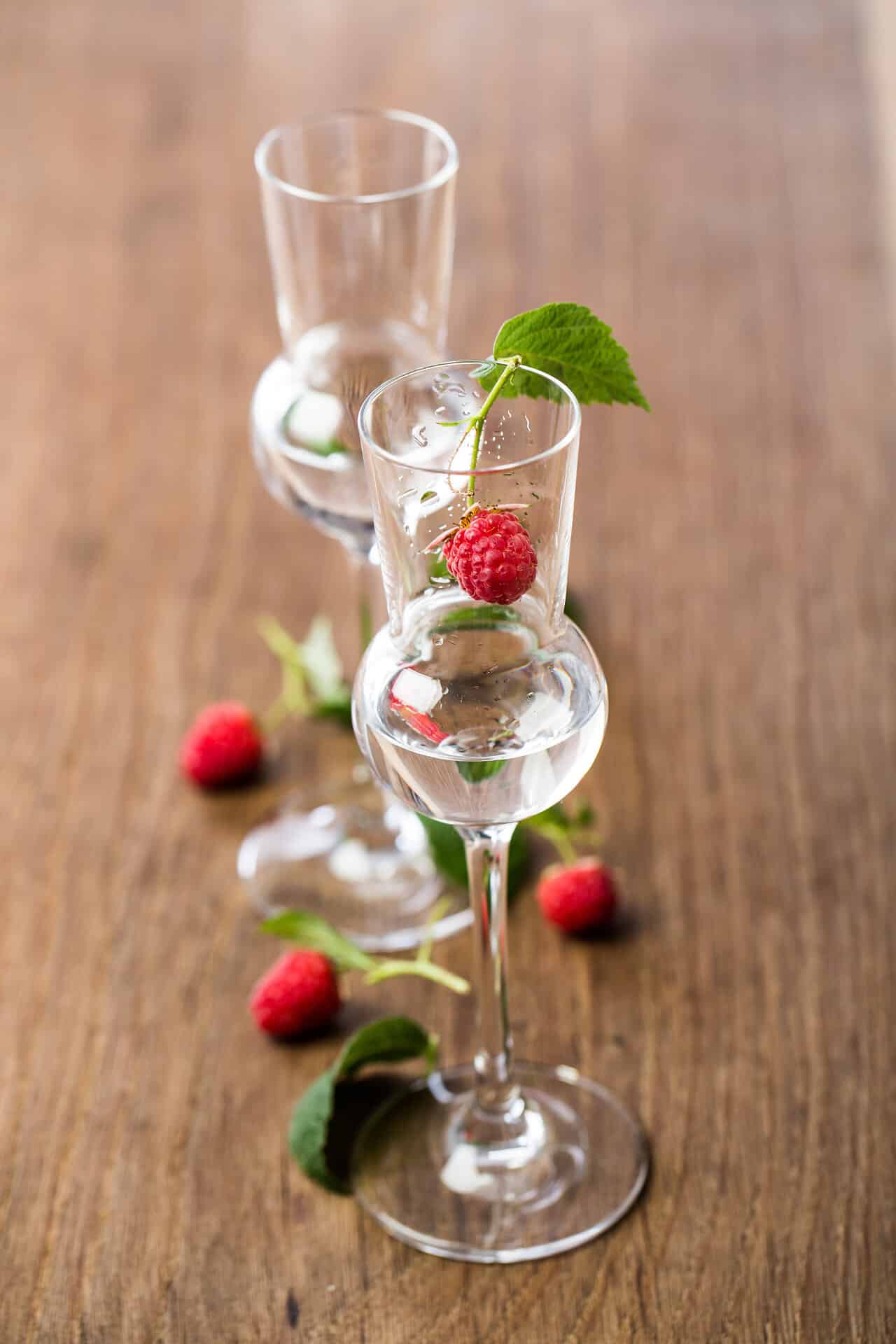 2 Gläser Himberschnaps 2 Gläser Himberschnaps auf einem Holztisch dekoriert mit kleinen Waldhimbeeren