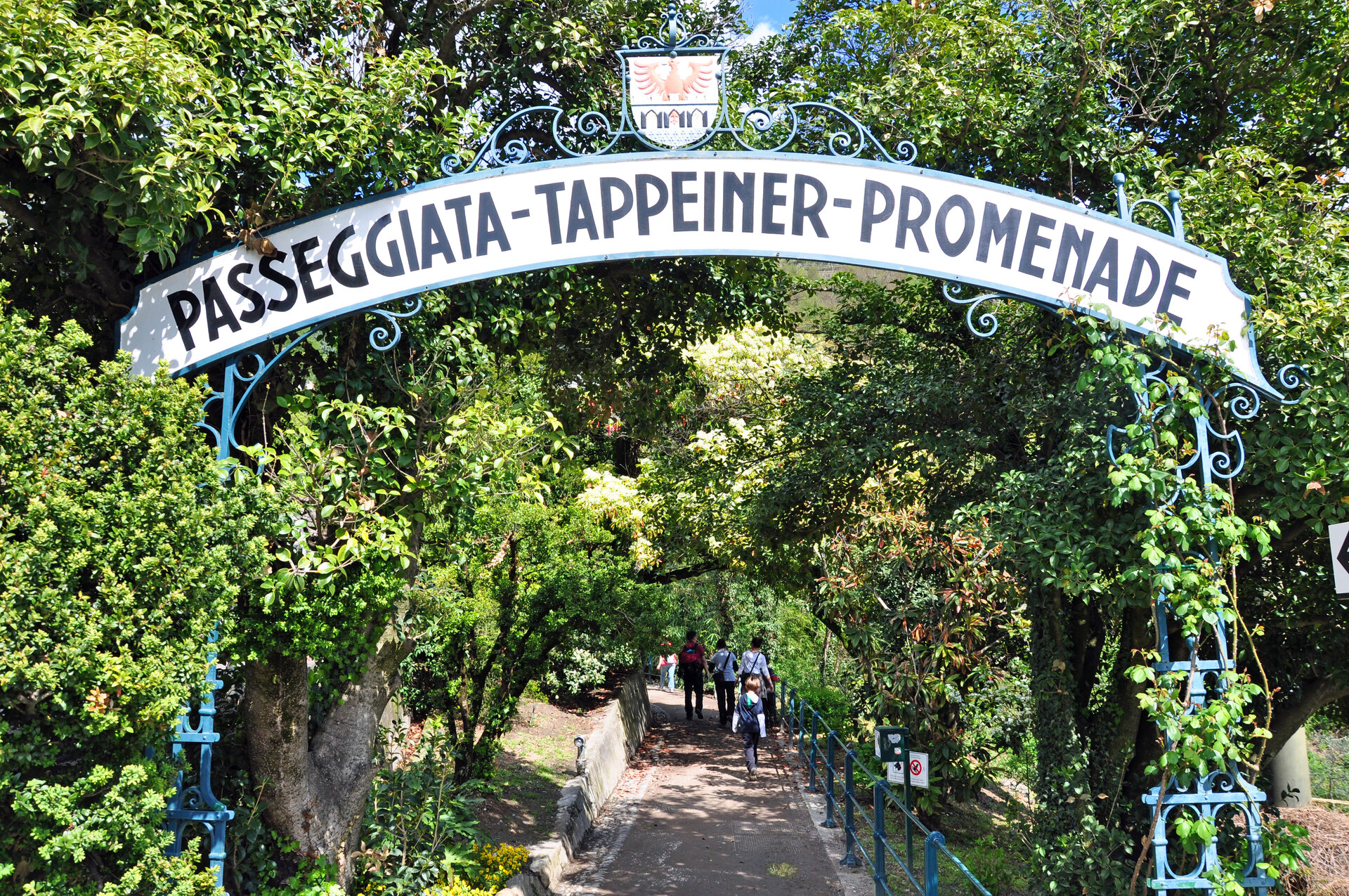 Tappeiner Weg Meran Rundes Bogenschild über Weg mit grünen Bäumen gesäumt mit der Aufschrift Passegiata-Tappeiner-Promenade