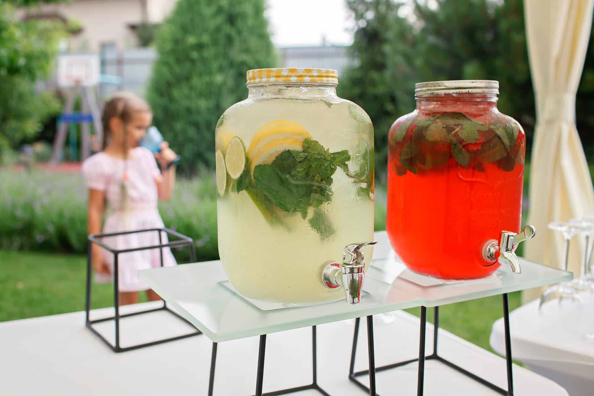 handmade lemonade Girl holding a glass of colorful natural fruits lemonade during backyard barbeque party at summer, elegant decoration, luxury catering, drink and buffet standing reception, festive celebration