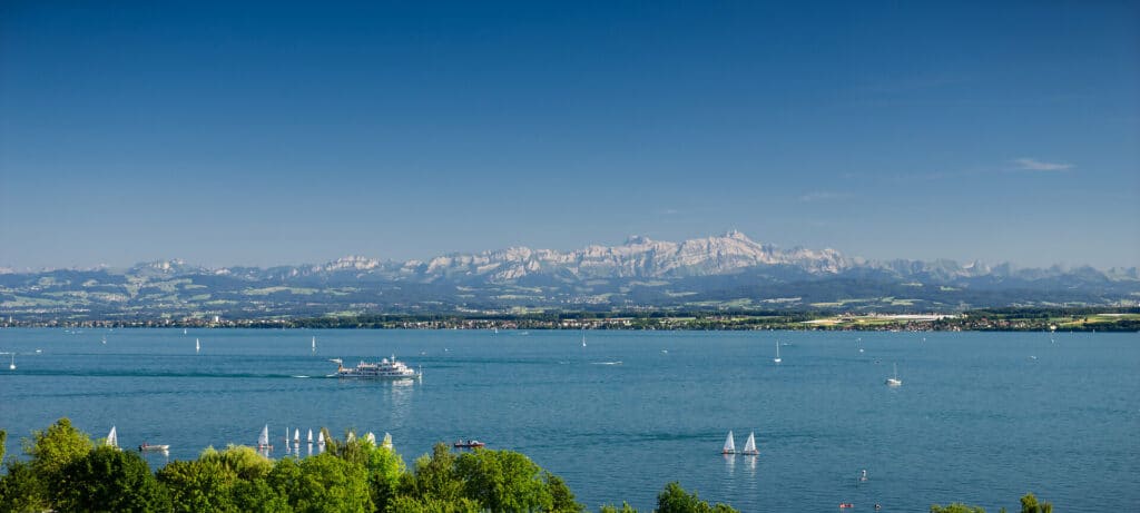 Der Bodensee Blick über den sommerlichen Bodensee auf das Säntisgebirge in der Schweiz mit Segelbooten und Ausflugsschiff.