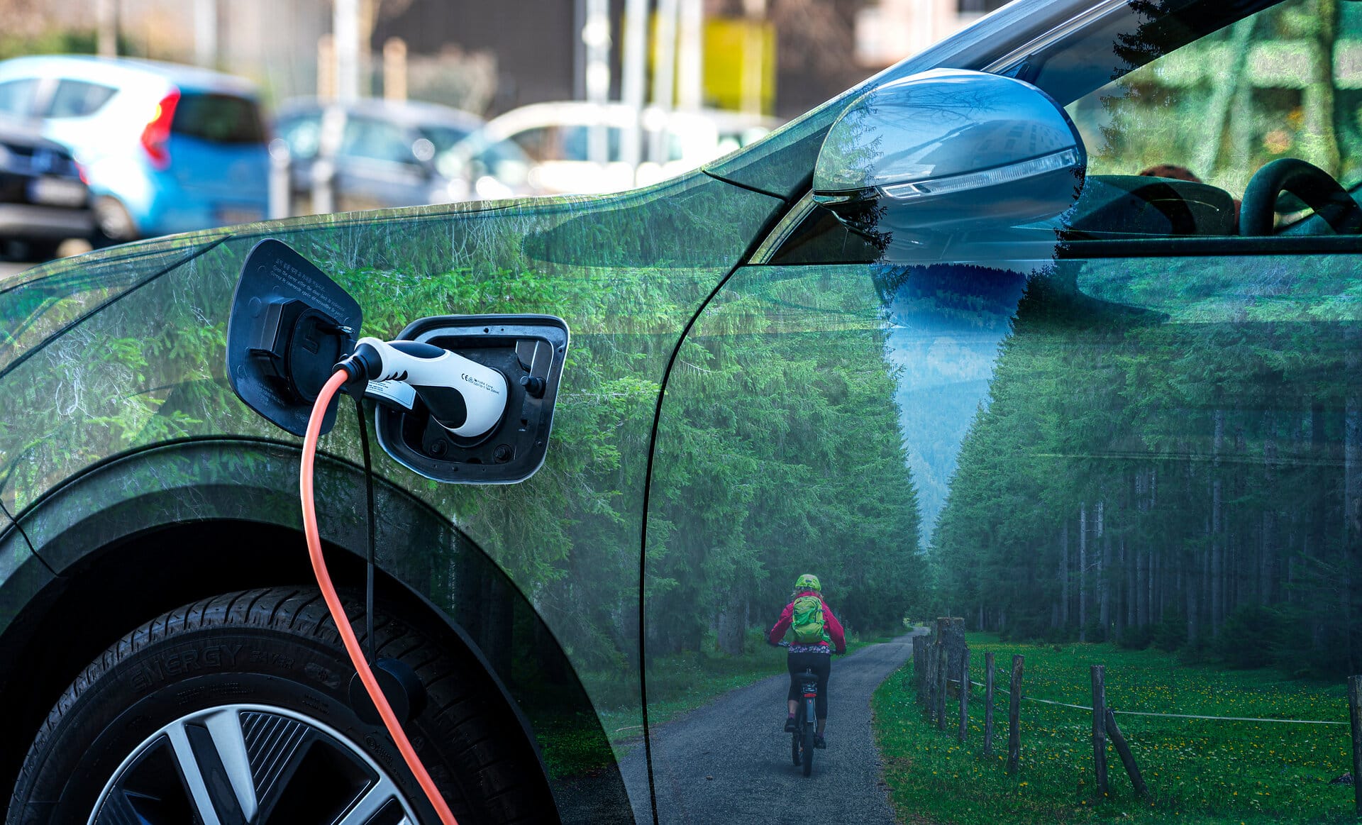 Ladekabel an einem Elektroauto Ladekabel an einem Elektroauto. Der glänzende Lack der Tür reflektiert einen Waldweg mit Radfahrer.