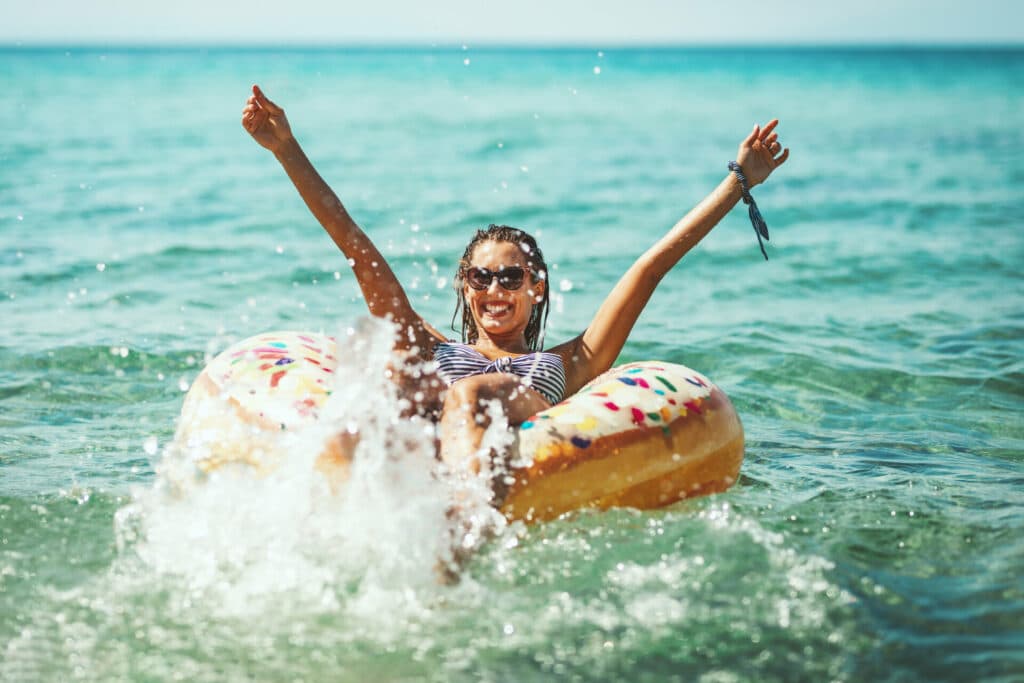 Summer Joy Junge Frau sitzt auf einem Schwimmriung im Meer und freut sich.