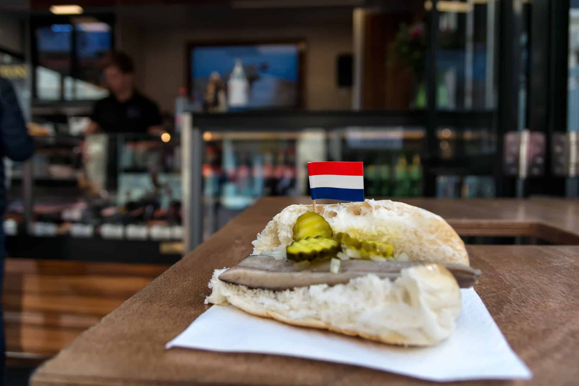 Dutch broodje haring Traditional dutch snack, seafood sandwich with herring, onions and pickled cucumber. Broodje haring on the wooden table. With flag of Netherlands.
